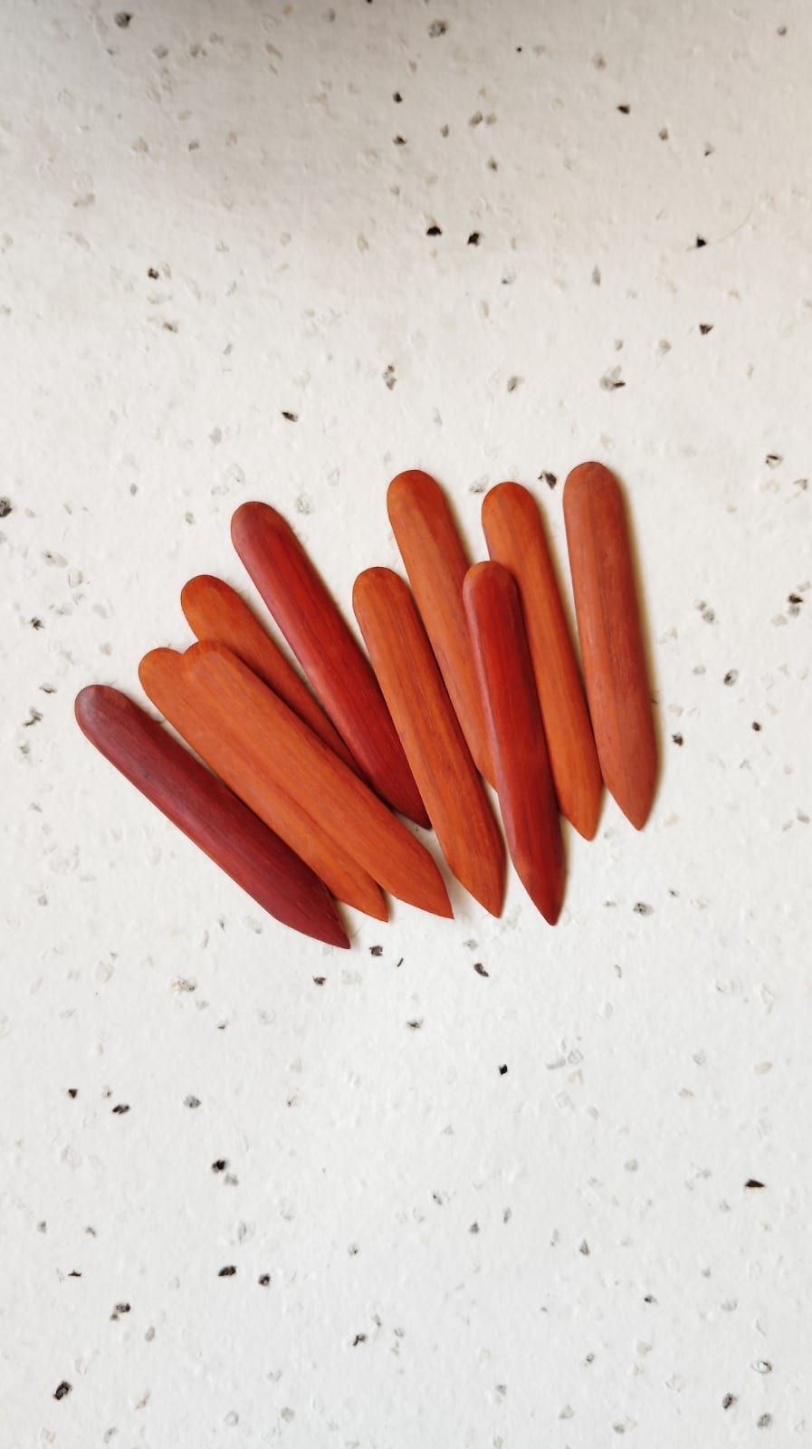 Set of nine handmade red-wood bone folders fanned on a speckled paper backdrop