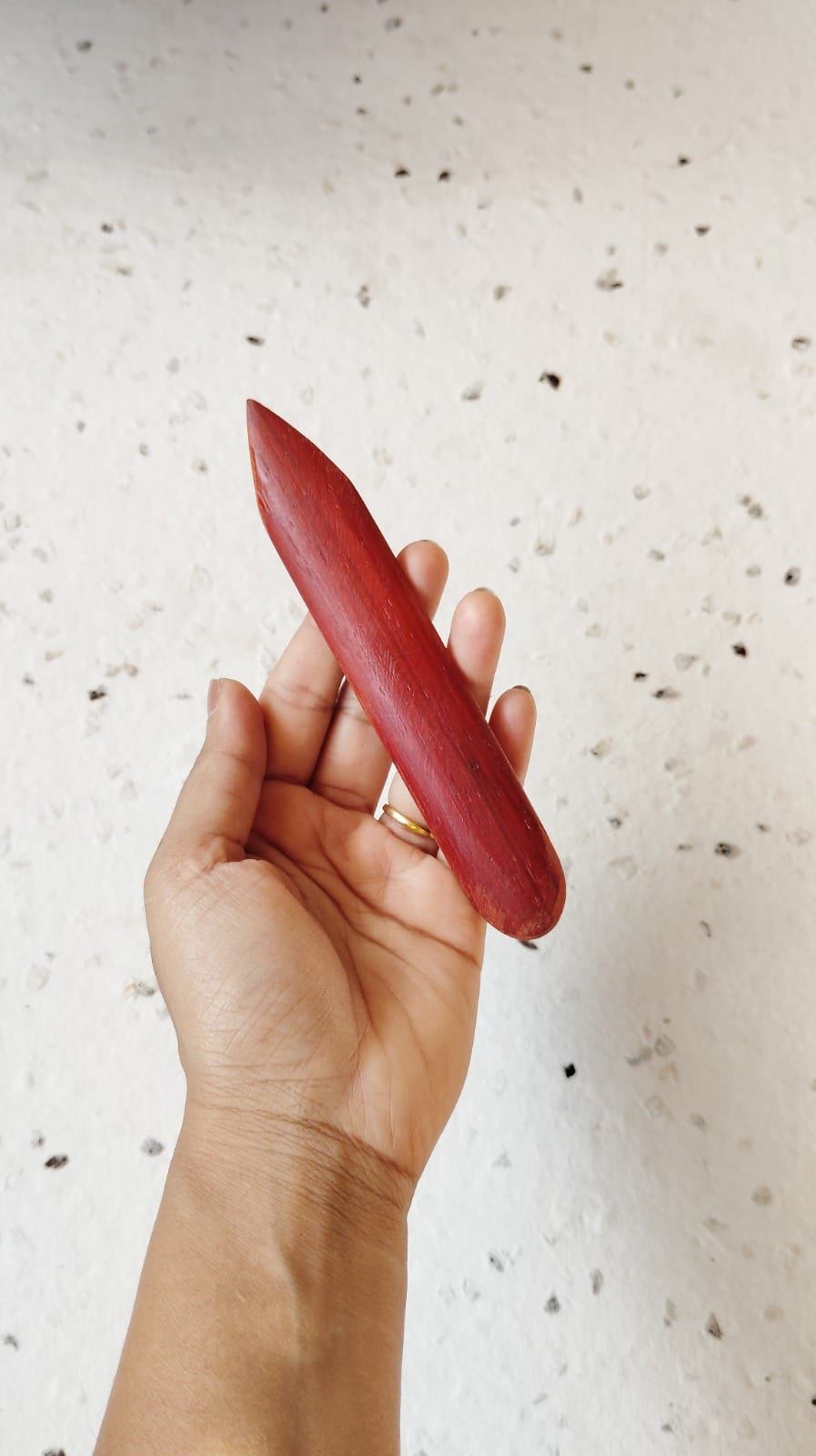 Red-wood bone folder held in hand showing polished tapered edge