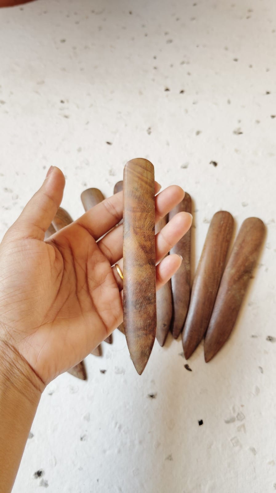 Walnut bone folder held in hand above a cluster of additional folders