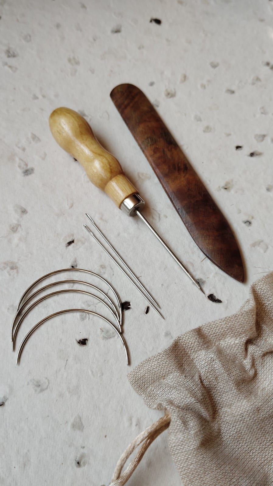 Bookbinding needle set with curved and straight needles beside an awl and bone folder